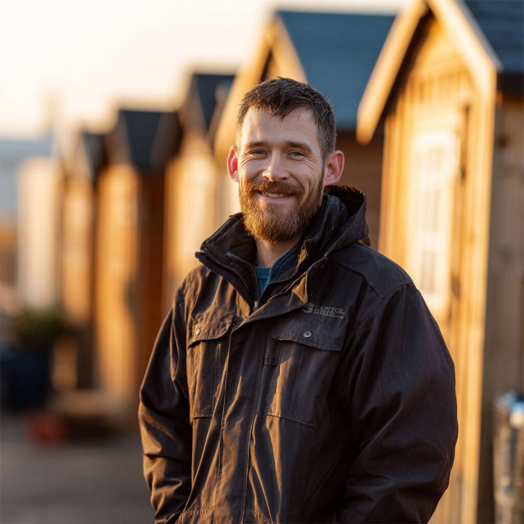 A Capitol Sheds employee standing in front of a line of sheds